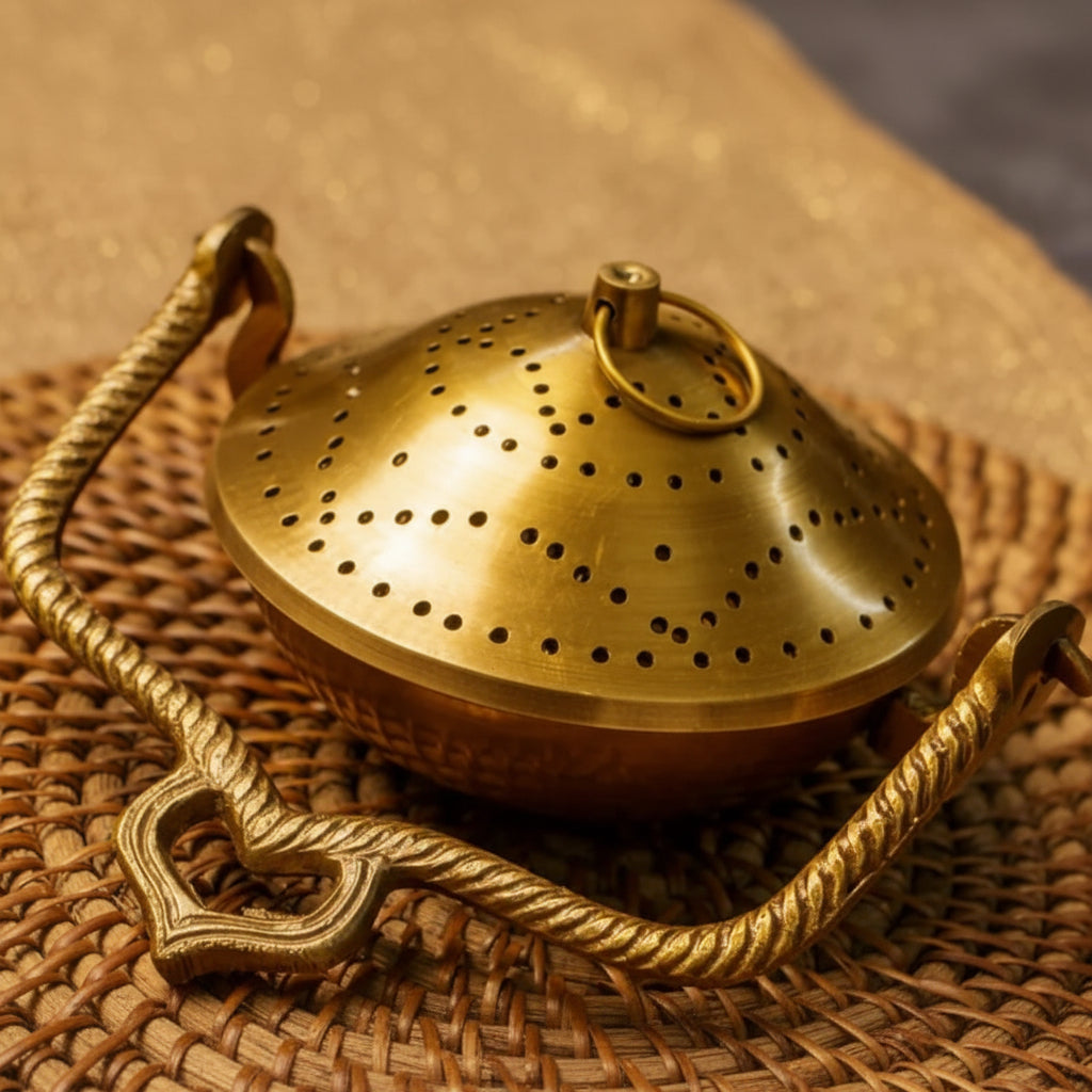 Brass tea strainer with decorative handle on a woven surface