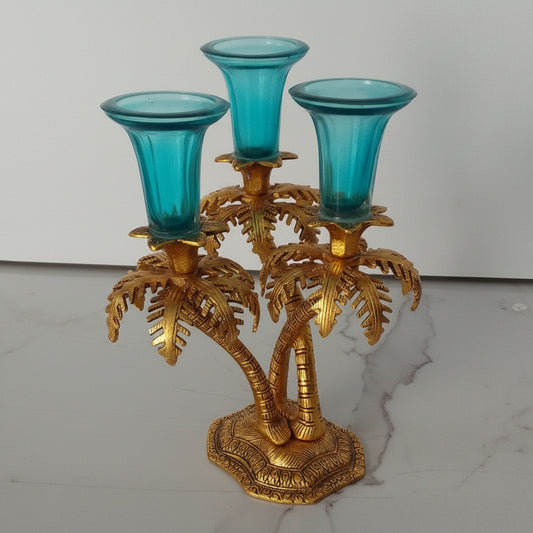 Decorative candelabrum with gold palm tree design and blue glass candle holders on a marble surface.
