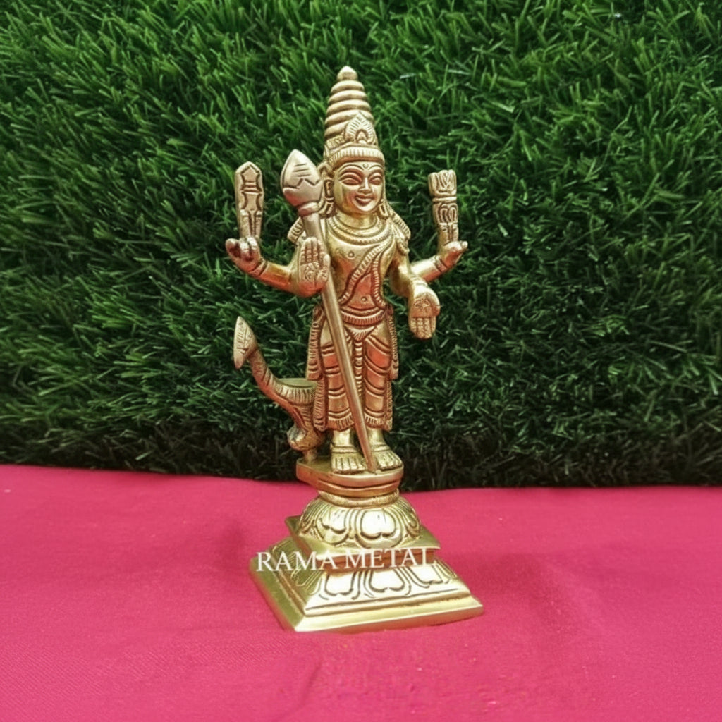 Brass statue of a deity on a pink surface with green grass background