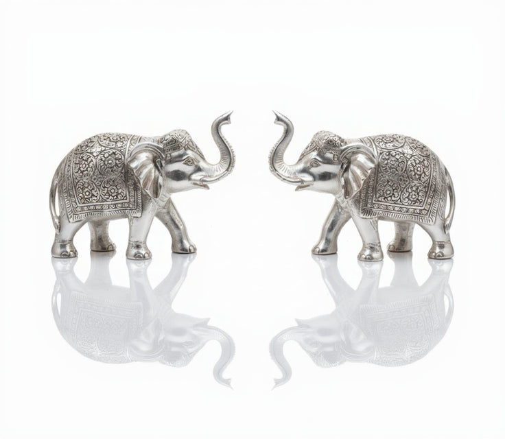 Two intricately designed silver elephants facing each other on a reflective surface.
