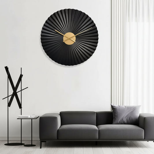 Decorative wall clock with black and gold design on a white wall above a gray sofa.