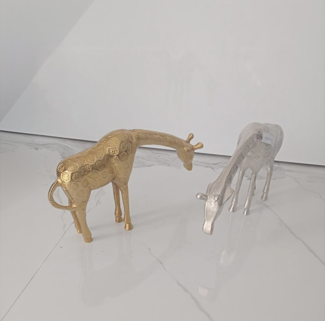 Gold and silver giraffe figurines on a reflective surface with a white background