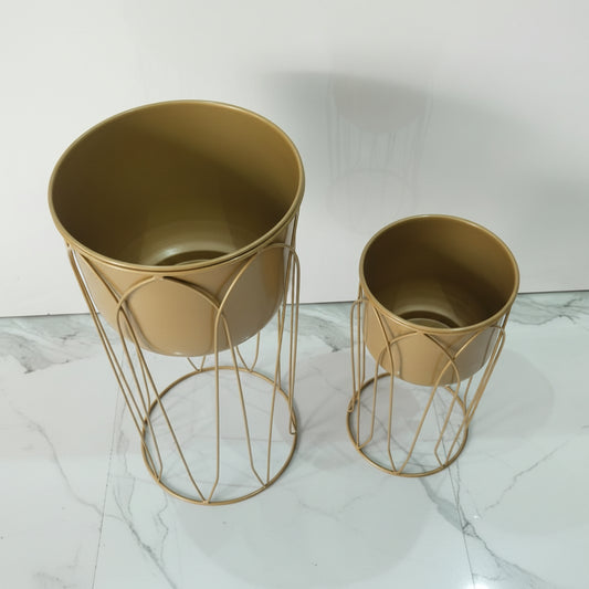 Two gold metal planters on a marble surface with a white background