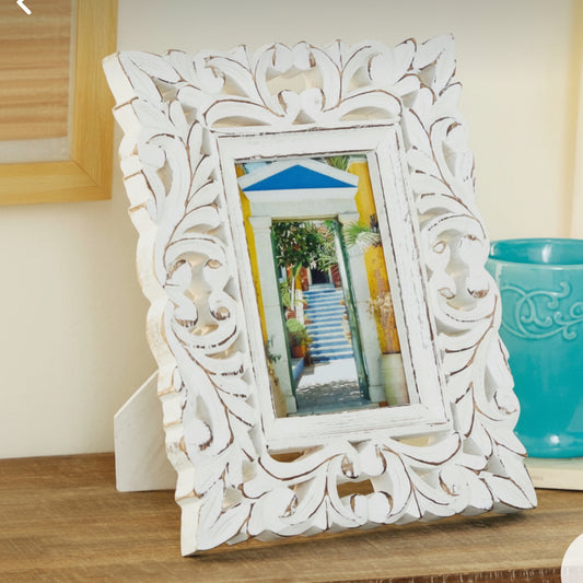 Decorative white frame with intricate carvings on a wooden surface.