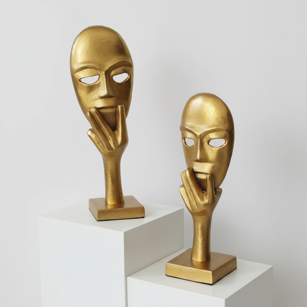 Two gold-colored masks on stands with a plain background