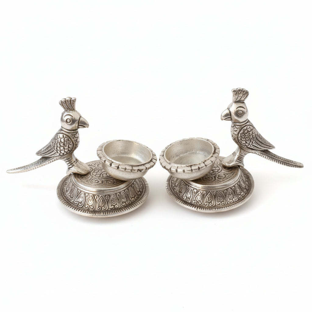 Decorative silver candle holders with bird designs on a reflective surface