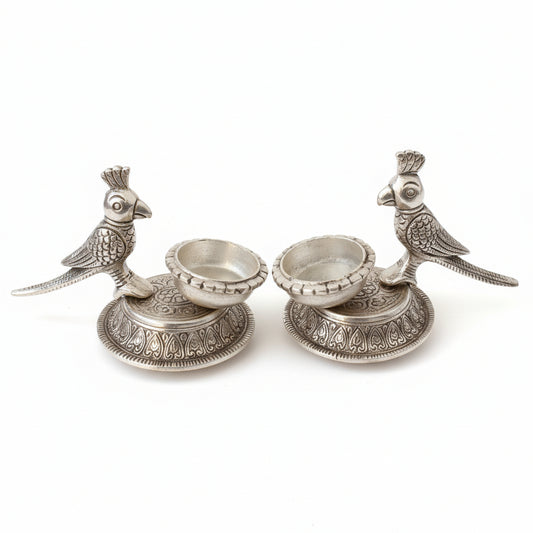 Decorative silver candle holders with bird designs on a reflective surface