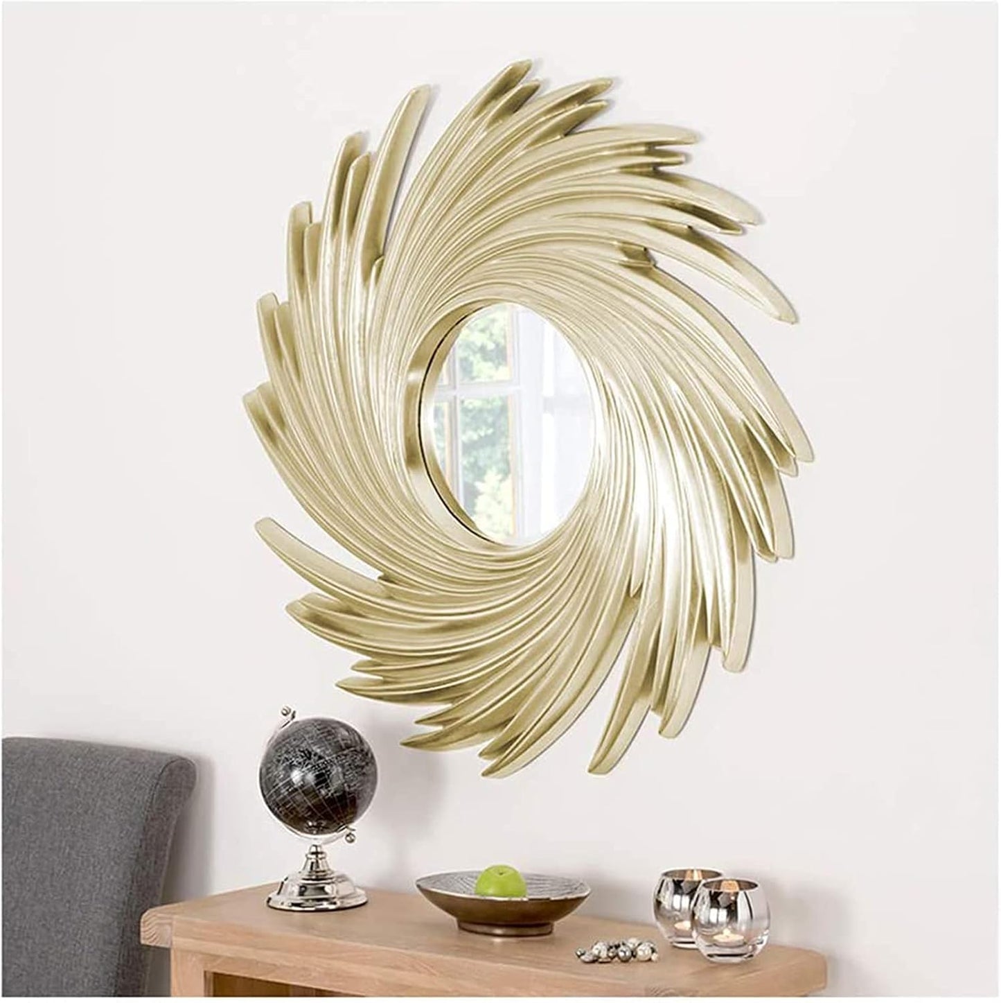 Decorative gold spiral wall mirror on a white wall with a table and small items below.