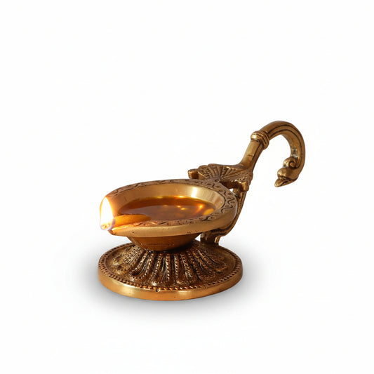 Decorative brass oil lamp with a lit candle on a wooden surface with white flowers in the background.