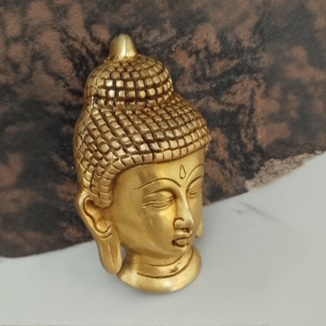 Gold-colored Buddha head sculpture on a marble surface with a brown textured background