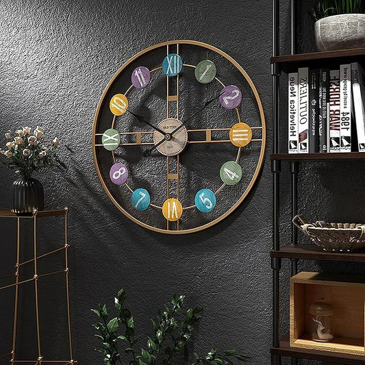 Decorative wall clock with colorful numbers on a dark gray wall, next to a bookshelf and small plant.