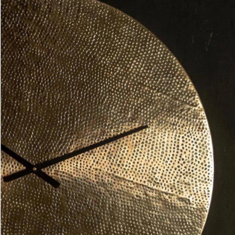 Gold textured wall clock with black hands on a dark background