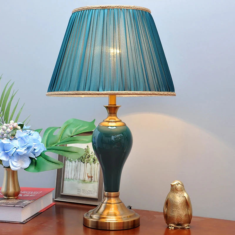 Decorative table lamp with a blue shade on a wooden surface with books and a penguin figurine.