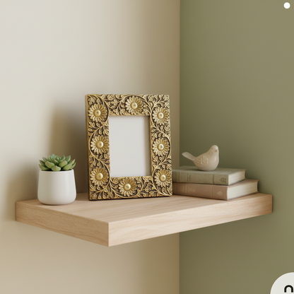 Decorative gold frame on a wooden shelf with a plant and books against a wall.