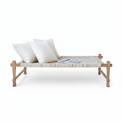 Wooden bench with white cushion and pillows against a white wall