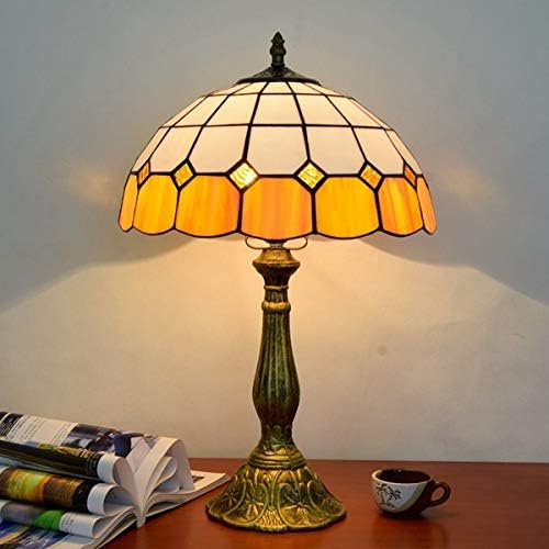 Tiffany-style table lamp with stained glass shade on a wooden surface with a cup and magazine.