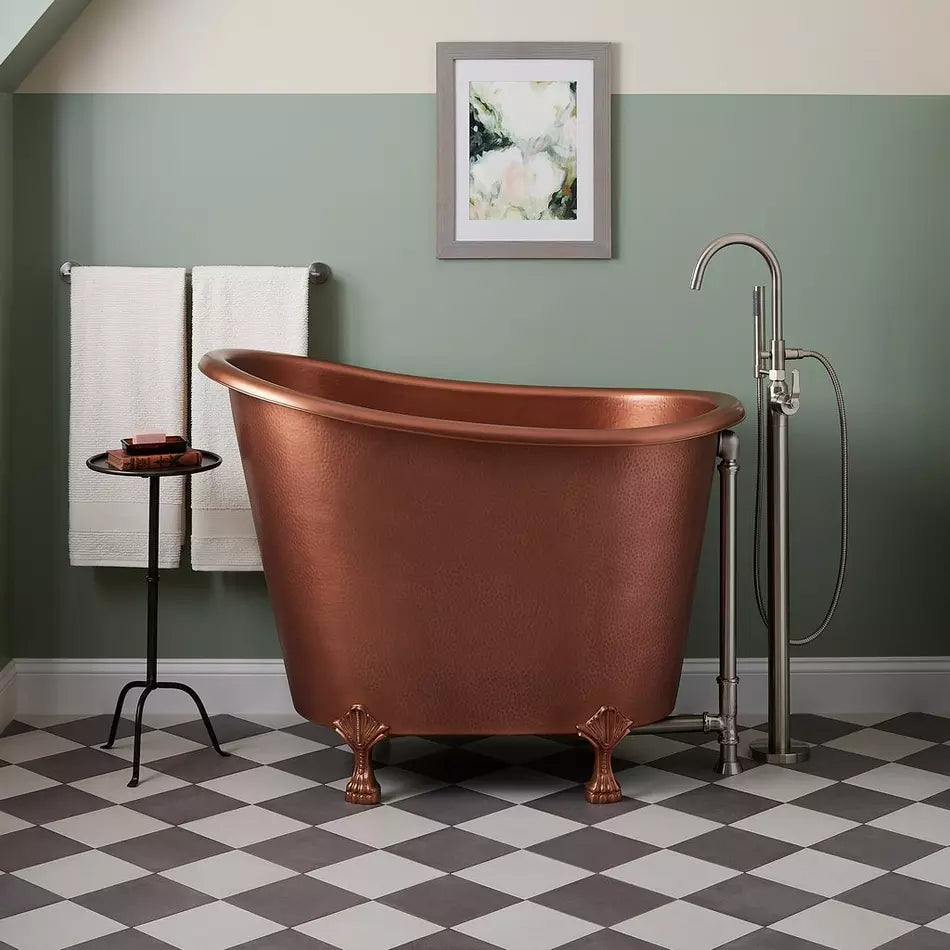 Copper bathtub in a bathroom with checkered floor and framed artwork on the wall.