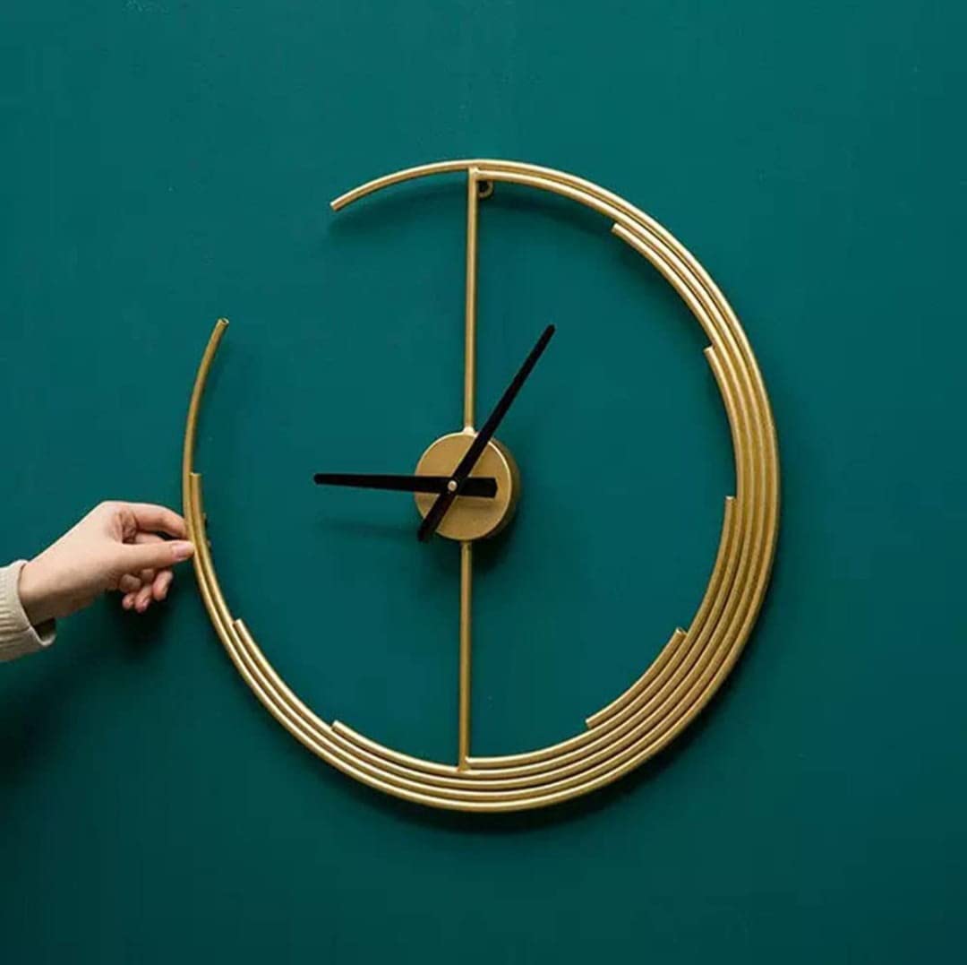 Gold wall clock on a teal background with a hand adjusting the time.