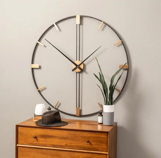 Large round wall clock on a plain wall with a wooden dresser below.