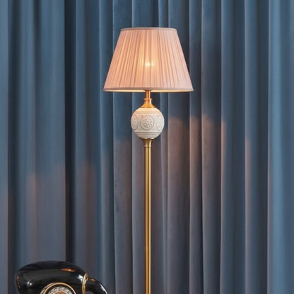 Decorative floor lamp with a gold base and a black lampshade against a dark curtain background.