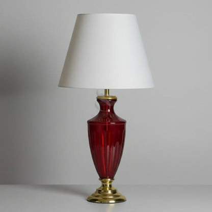 Table lamp with red glass base and white shade on a gray background