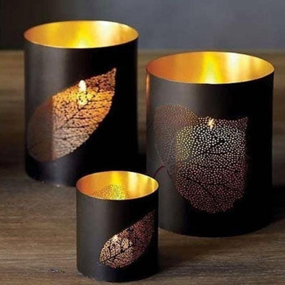 Three black candle holders with gold interior and leaf patterns on a wooden surface.