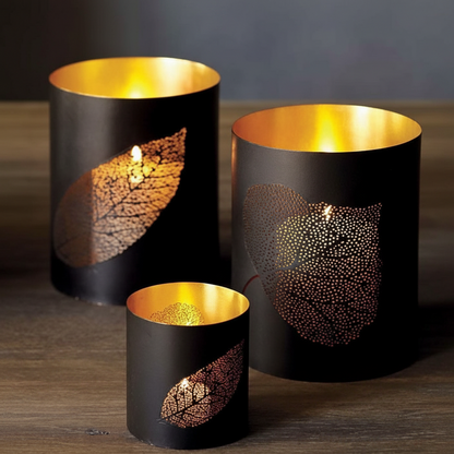 Three black candle holders with gold interior and leaf patterns on a wooden surface.