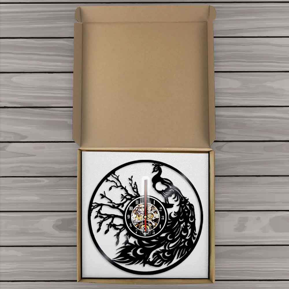 Decorative wall clock with peacock design inside a cardboard box on a wooden surface