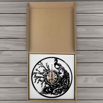 Decorative wall clock with peacock design inside a cardboard box on a wooden surface