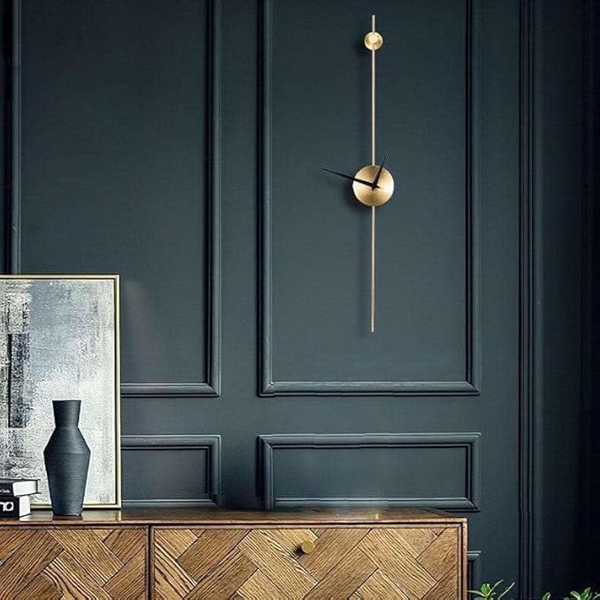 Modern wall clock on a dark green wall with wooden cabinet and framed artwork.