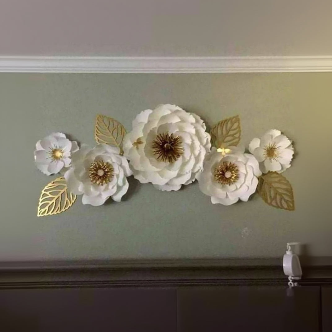 Decorative wall art with white flowers and gold leaves on a light green wall.