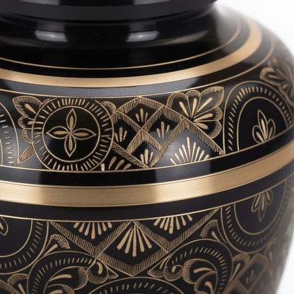 Close-up of a black urn with gold intricate patterns on a white background
