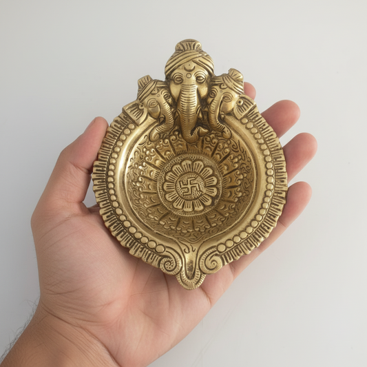 Hand holding a decorative brass plaque with elephant design against a white background