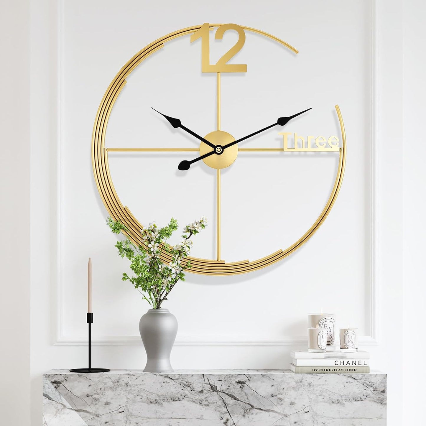 Gold wall clock on a white wall with decorative items below.