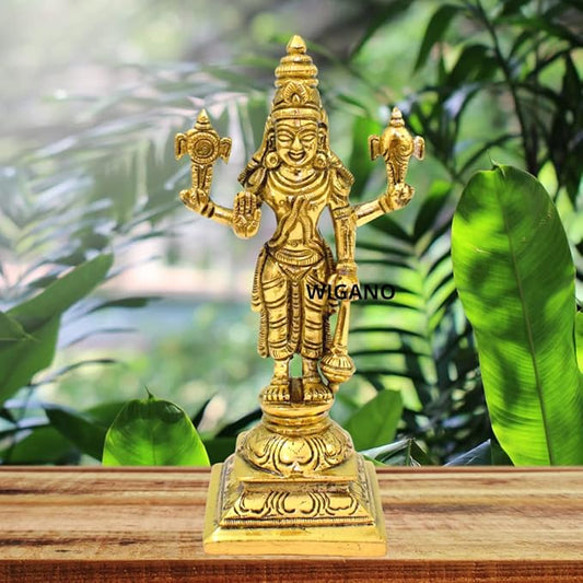Gold-colored statue of a deity on a wooden surface with green leaves in the background