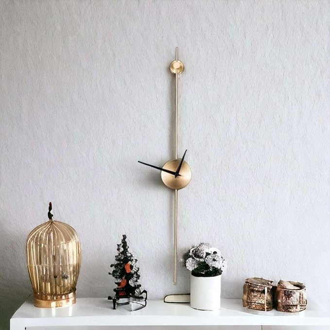 Decorative wall clock with a long gold pendulum on a white surface with small decorative items.