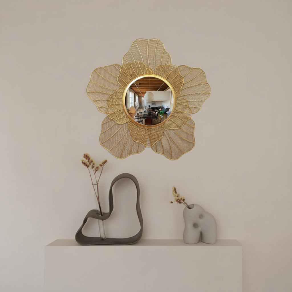 Decorative wall mirror with floral design on a white wall above a shelf with sculptures.
