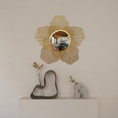 Decorative wall mirror with floral design on a white wall above a shelf with sculptures.