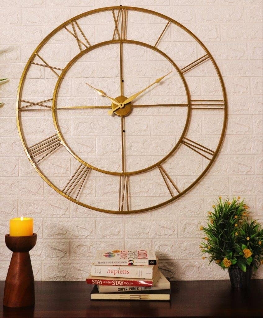 Gold wall clock on a textured wall with books and a candle below.