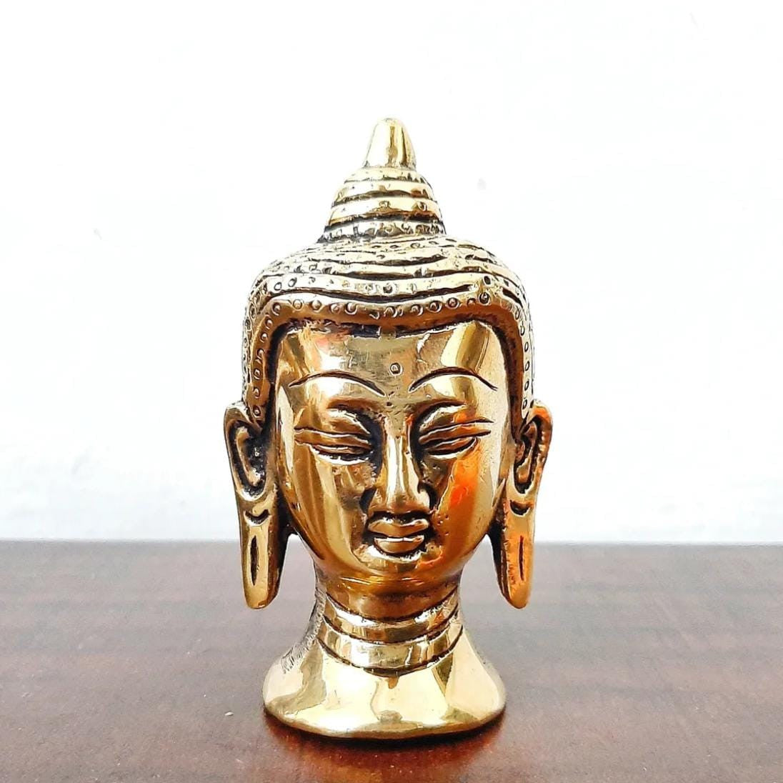 Gold-colored Buddha head statue on a wooden surface with a white background
