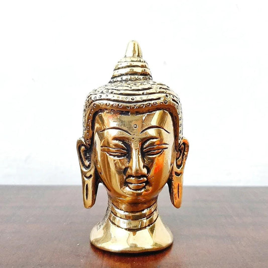 Gold-colored Buddha head statue on a wooden surface with a white background