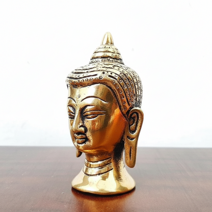 Gold Buddha head figurine on a wooden surface with a white background