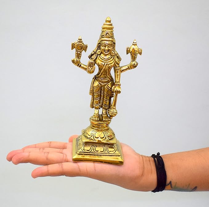 Gold-colored statue of a deity held in a hand against a plain background