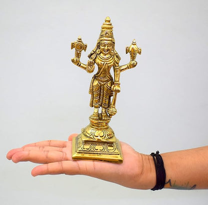 Gold-colored statue of a deity held in a hand against a plain background