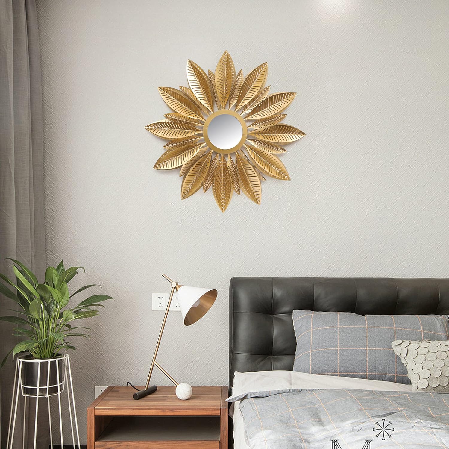 Decorative gold sunburst mirror on a wall above a bed with a nightstand and plant.