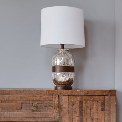 Table lamp with a decorative glass base on a wooden cabinet against a gray wall