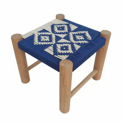 Small wooden stool with a blue and white woven seat on a stone pavement.