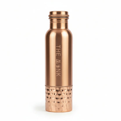Rose gold water bottle with 'The Monk' branding in a black box on a wooden surface.