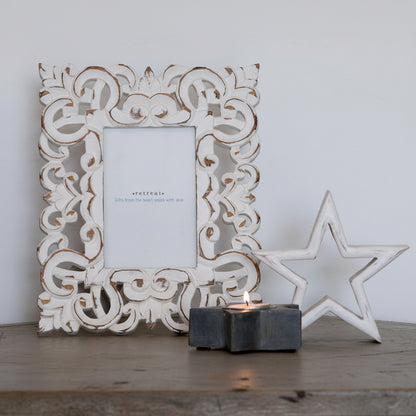 Decorative white frame with intricate patterns, a star-shaped object, and a candle on a wooden surface.