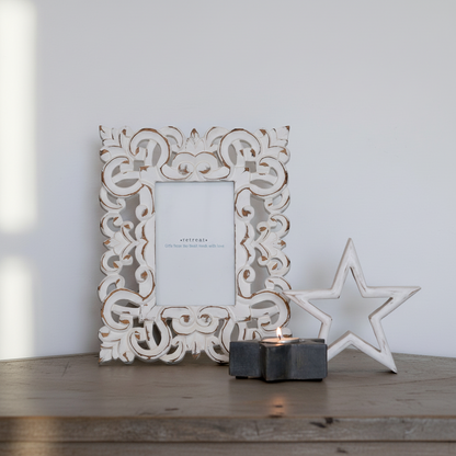 Decorative white frame with intricate patterns on a wooden surface with a star and candle.
